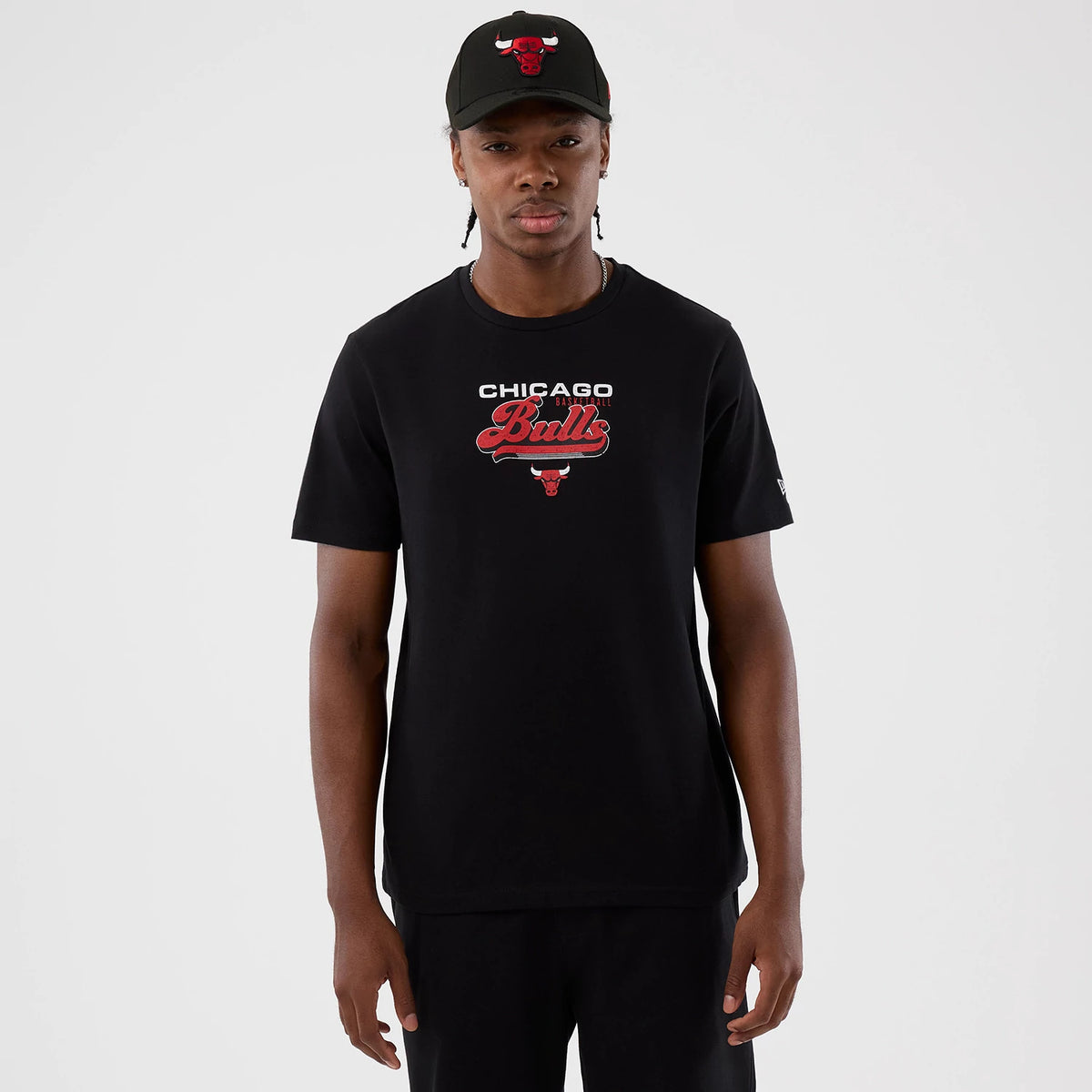 New Era Chicago Bulls NBA Back To School Black T-Shirt, front view on a model wearing a matching black cap, displaying printed Chicago Bulls lettering and the team logo on the chest, with a small embroidered New Era flag on the sleeve.