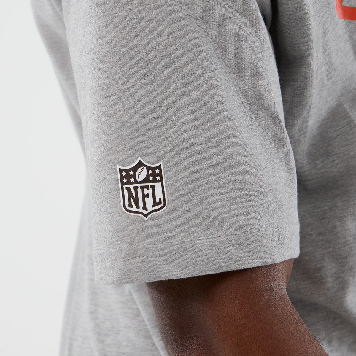 New Era Cleveland Browns NFL International Series Games Grey Oversized T-Shirt, three-quarter view showing a white printed NFL shield logo on the left sleeve, highlighting the shirt's relaxed fit and design detail.