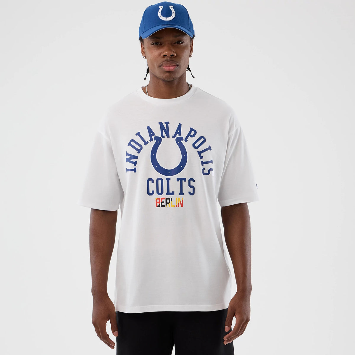 New Era Indianapolis Colts NFL International Series Games White Oversized T-Shirt, front view on a model with a blue cap, featuring blue Indianapolis Colts lettering with a horseshoe graphic and Berlin text in small coloured print.