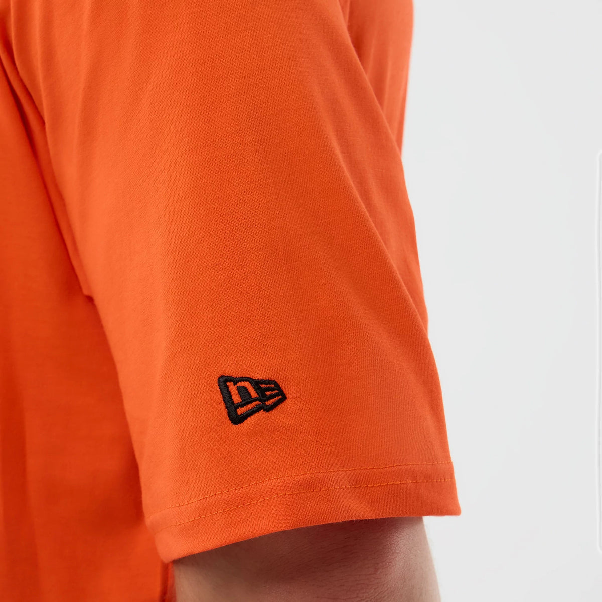 New Era Cleveland Browns NFL International Series Games Orange Oversized T-Shirt, three-quarter view highlighting the sleeve with an embroidered black New Era logo near the cuff on the orange fabric.