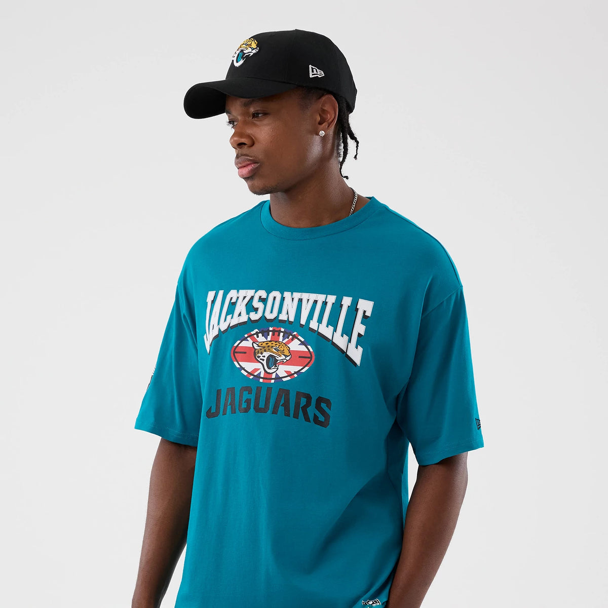 New Era Jacksonville Jaguars NFL International Series Games Turquoise Oversized T-Shirt, front view on a model with a black cap, showcasing Jacksonville lettering above a large Jaguars logo graphic centred on the chest.