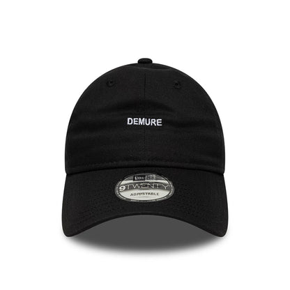 New Era Slogan Demure Black 9TWENTY Adjustable Cap, front view showing the white embroidered DEMURE text on the structured black crown, with a curved visor and 9TWENTY size sticker.