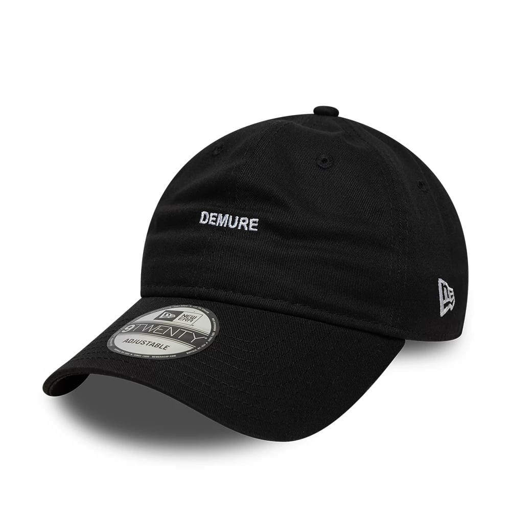 New Era Slogan Demure Black 9TWENTY Adjustable Cap, front view with white Demure embroidery on the unstructured black crown, a curved visor with a 9TWENTY size sticker, and New Era flag logo on the left side.