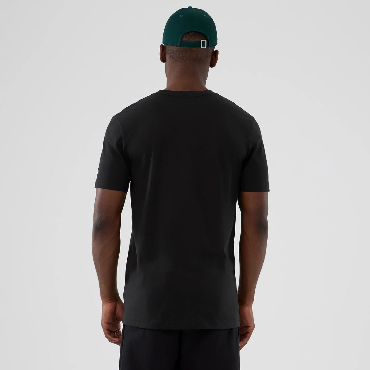 New Era Minnesota Timberwolves NBA Hardwood Classic Black T-Shirt, back view on a model styled with dark shorts and a green cap, showing a plain black back with short sleeves and a embroidered New Era logo on the left sleeve.