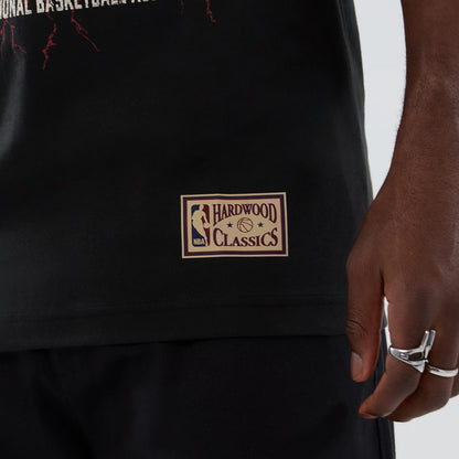 New Era Denver Nuggets NBA Hardwood Classic Black T-Shirt, side view showing a beige printed NBA Hardwood Classics patch near the hem, with parts of red lightning graphics above, styled on a model wearing black trousers.
