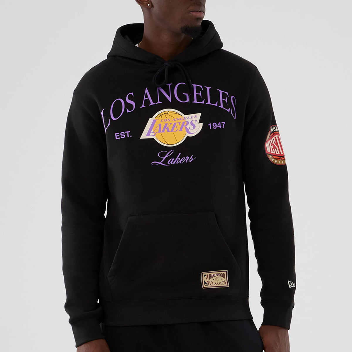 New Era LA Lakers NBA Hardwood Classic Black Pullover Hoodie, front view on-model showing the purple Los Angeles Lakers graphic across the chest, a Western Conference patch on the left sleeve, and a New Era logo embroidered near the cuff.