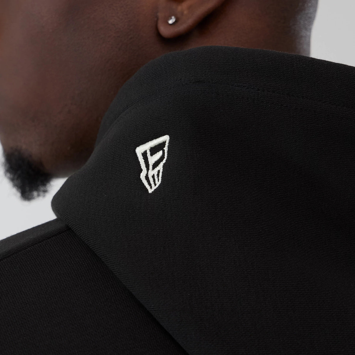 New Era LA Lakers NBA Hardwood Classic Black Pullover Hoodie, three-quarter view of the black hood with an embroidered white logo near the edge, shown on a model with the focus on the shoulder area.