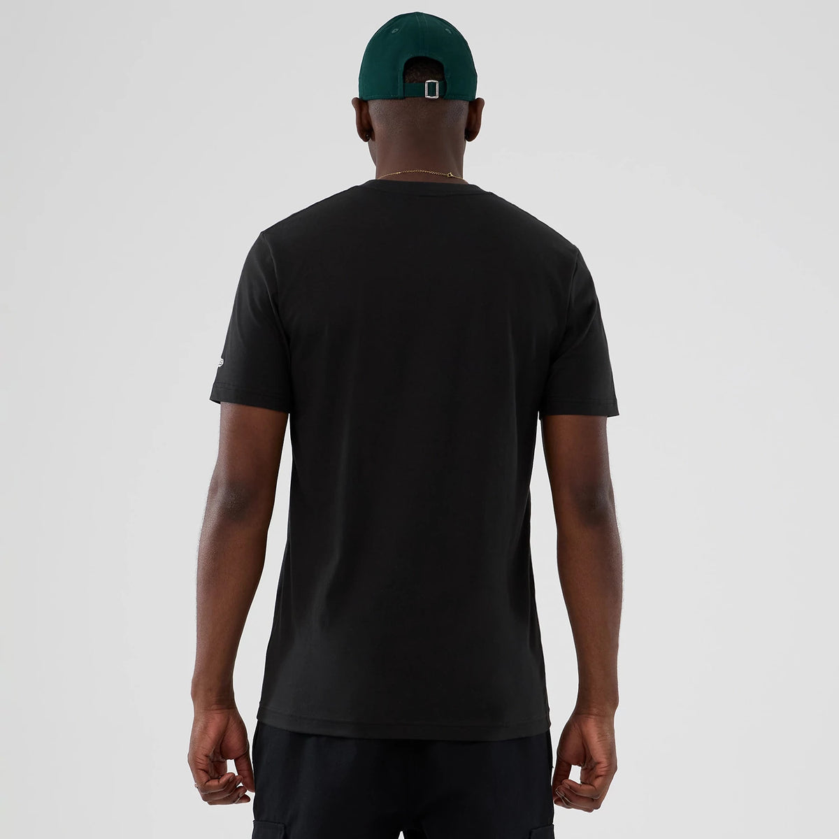 New Era Seattle Supersonics NBA Hardwood Classic Black T-Shirt, back view on a model with a green cap, showing plain black fabric with a embroidered New Era logo on the left sleeve near the cuff.