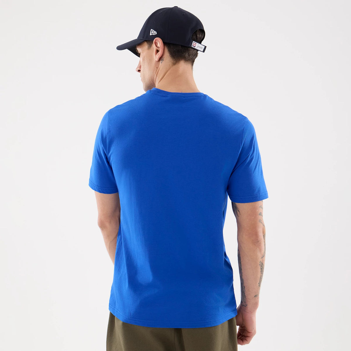 New Era New York Yankees MLB Blue T-Shirt, back view on a model showing the plain blue back panel, short sleeves, and rounded neckline, worn with a dark cap featuring an embroidered New Era logo on the side and a white patch on the back strap.