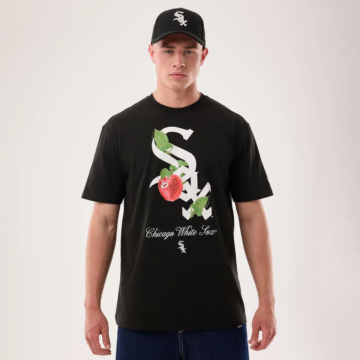 New Era Chicago White Sox MLB Life Graphic Black T-Shirt, front view on a model styled with a matching cap, featuring a large white team logo combined with a red apple graphic and the words Chicago White Sox printed below it.