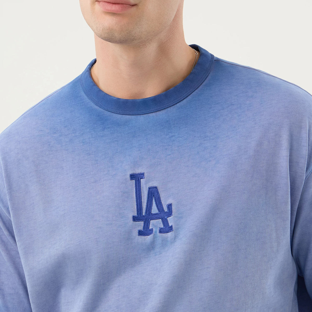 New Era LA Dodgers MLB Washed Logo Pastel Blue T-Shirt, front view on-model showing the upper chest and shoulders, with an embroidered LA Dodgers logo in a deeper blue at the centre, and a gradient from light to dark blue across the t-shirt.