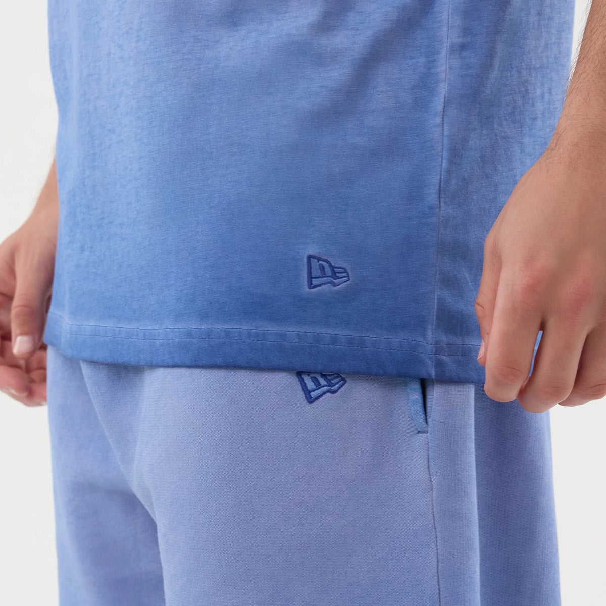 New Era LA Dodgers MLB Washed Logo Pastel Blue Vest, on-model close-up showing the delicate blue wash texture, an embroidered New Era flag logo near the bottom hem, and a glimpse of matching pastel blue shorts below.