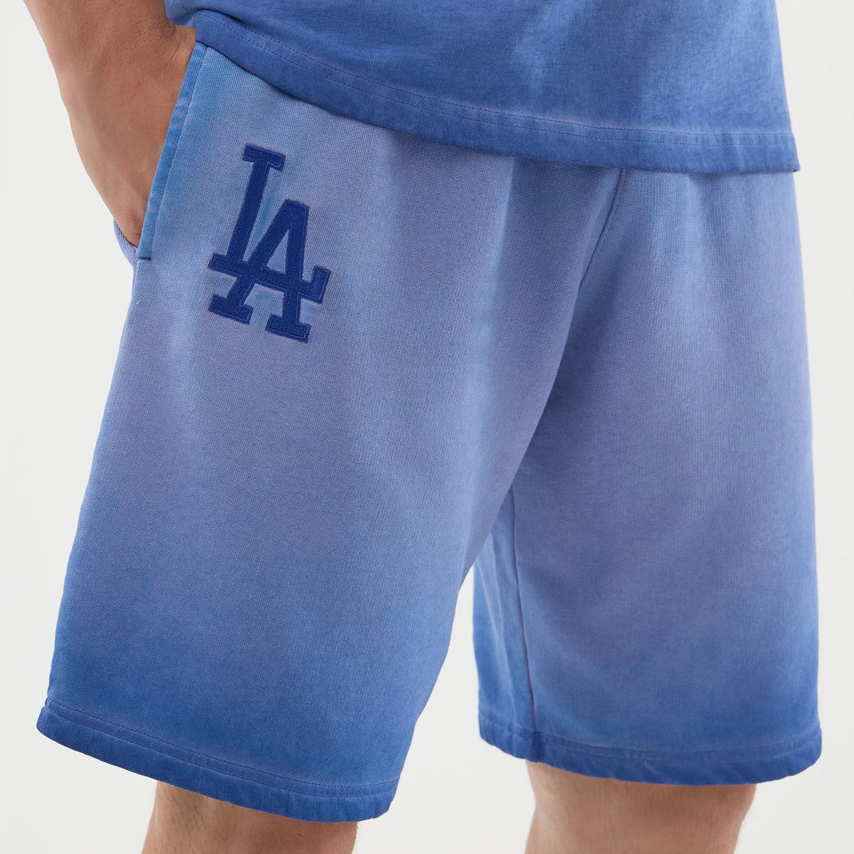 New Era LA Dodgers MLB Washed Logo Pastel Blue Shorts, front view showing a model wearing pastel blue shorts with a gradient effect, side pockets, and an embroidered blue LA Dodgers logo on the left leg, styled with a coordinating blue top.