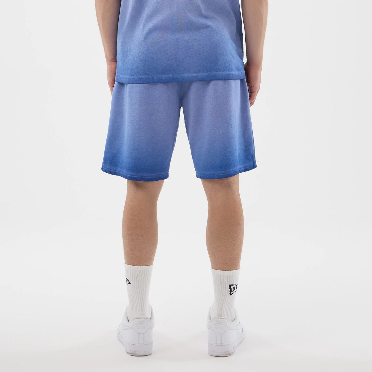 New Era LA Dodgers MLB Washed Logo Pastel Blue Shorts, back view on a model with a blue gradient matching shirt, featuring a wash effect across the shorts and a relaxed fit, complemented by plain white socks and white trainers.