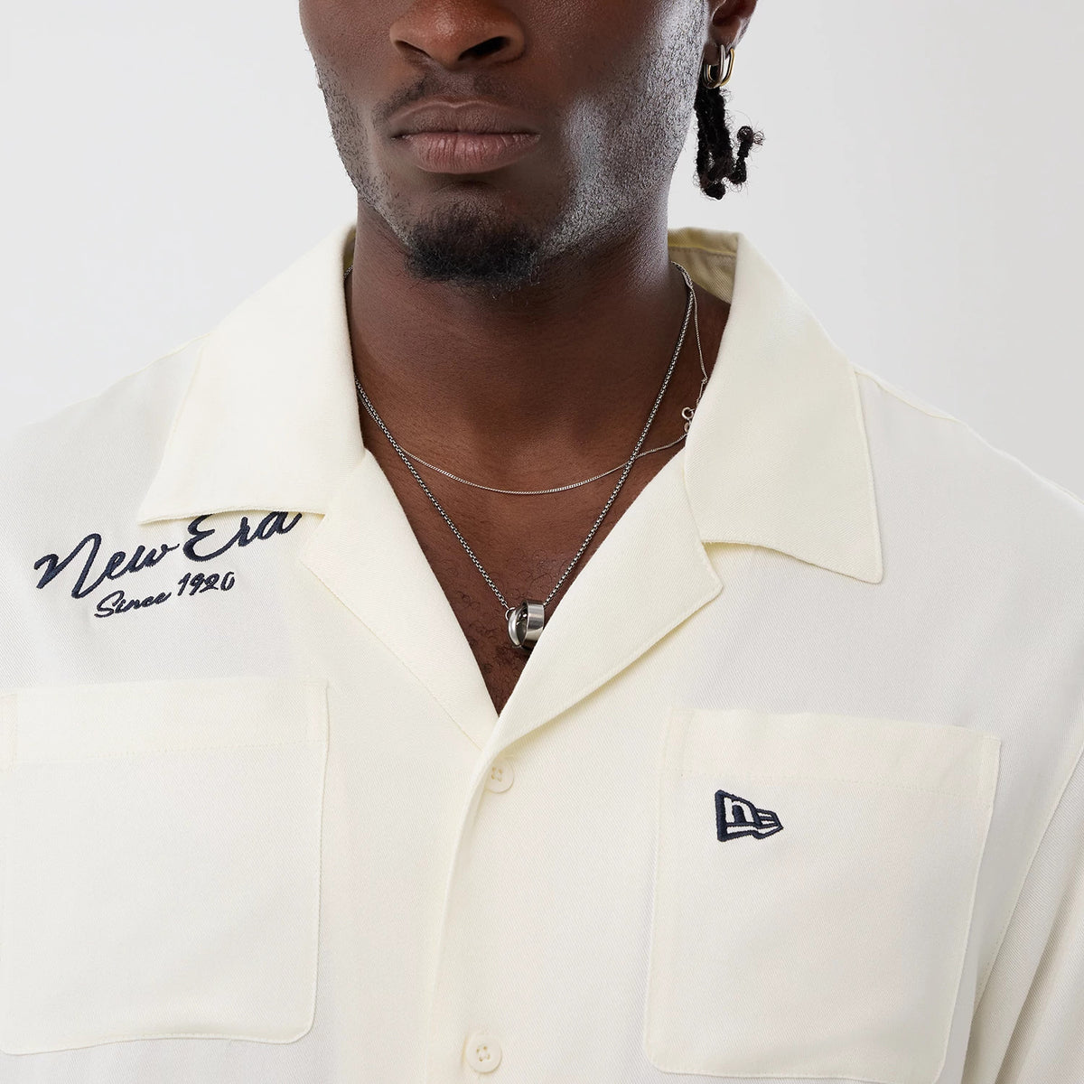 The model is wearing this New Era Graphic Revere Short Sleeve Shirt in open white. 5