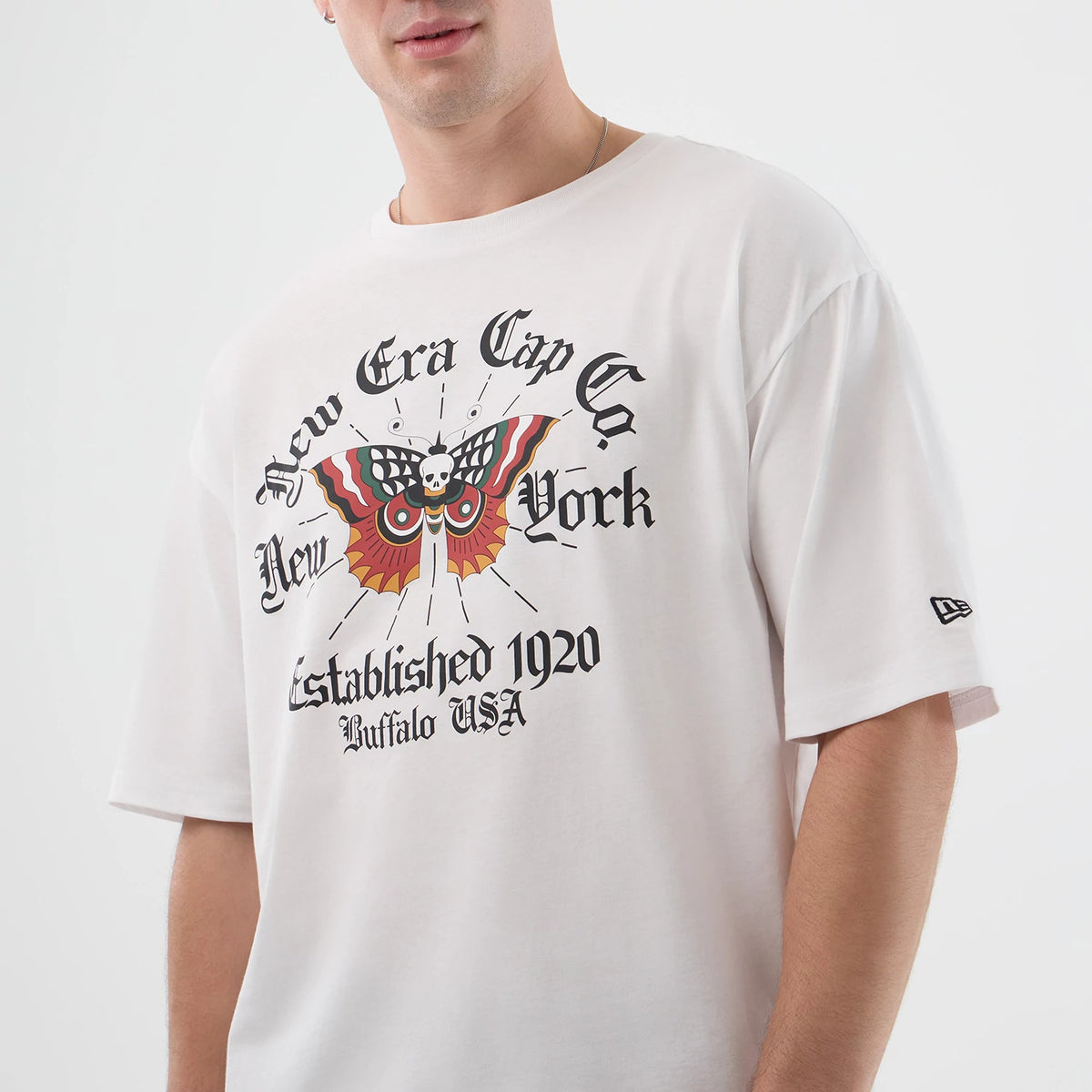 New Era Death Moth Graphic White Oversized T-Shirt, front view on a model showing a death moth motif in vivid colours with text reading New Era Cap Co New York and Established 1920 Buffalo USA, and an embroidered New Era logo on the sleeve.