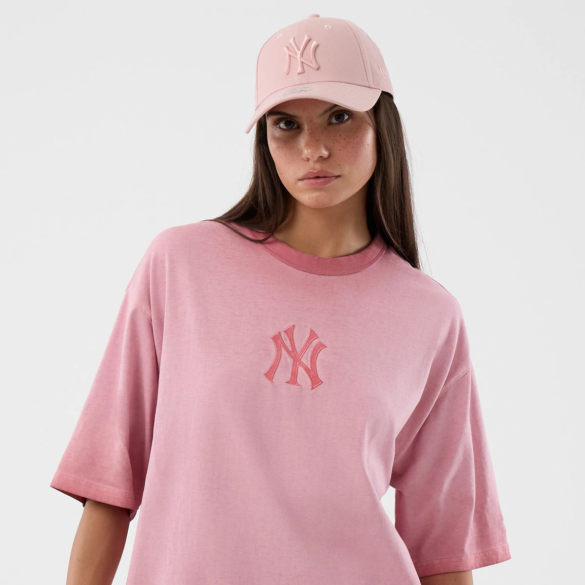 New Era New York Yankees MLB Washed Logo Pastel Pink T-Shirt, front view on a model wearing a matching cap, showing the embroidered New York Yankees logo centred on the chest against the soft pastel pink background with short relaxed sleeves.