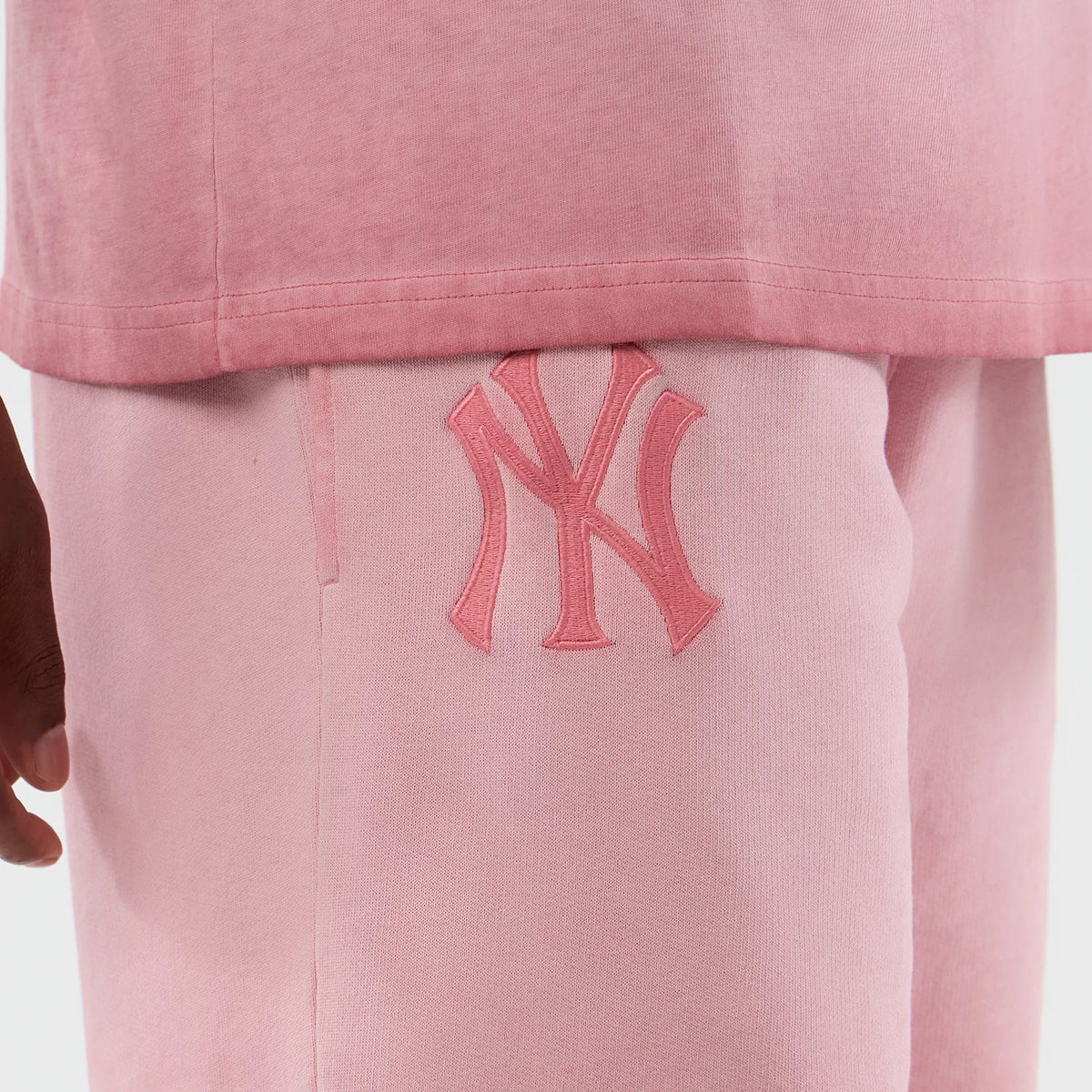 New Era New York Yankees MLB Washed Logo Pastel Pink Shorts, front view showing a large embroidered NY logo on the left thigh, the soft pastel pink fabric contrasting with a slightly darker pink shirt edge above the waistband.