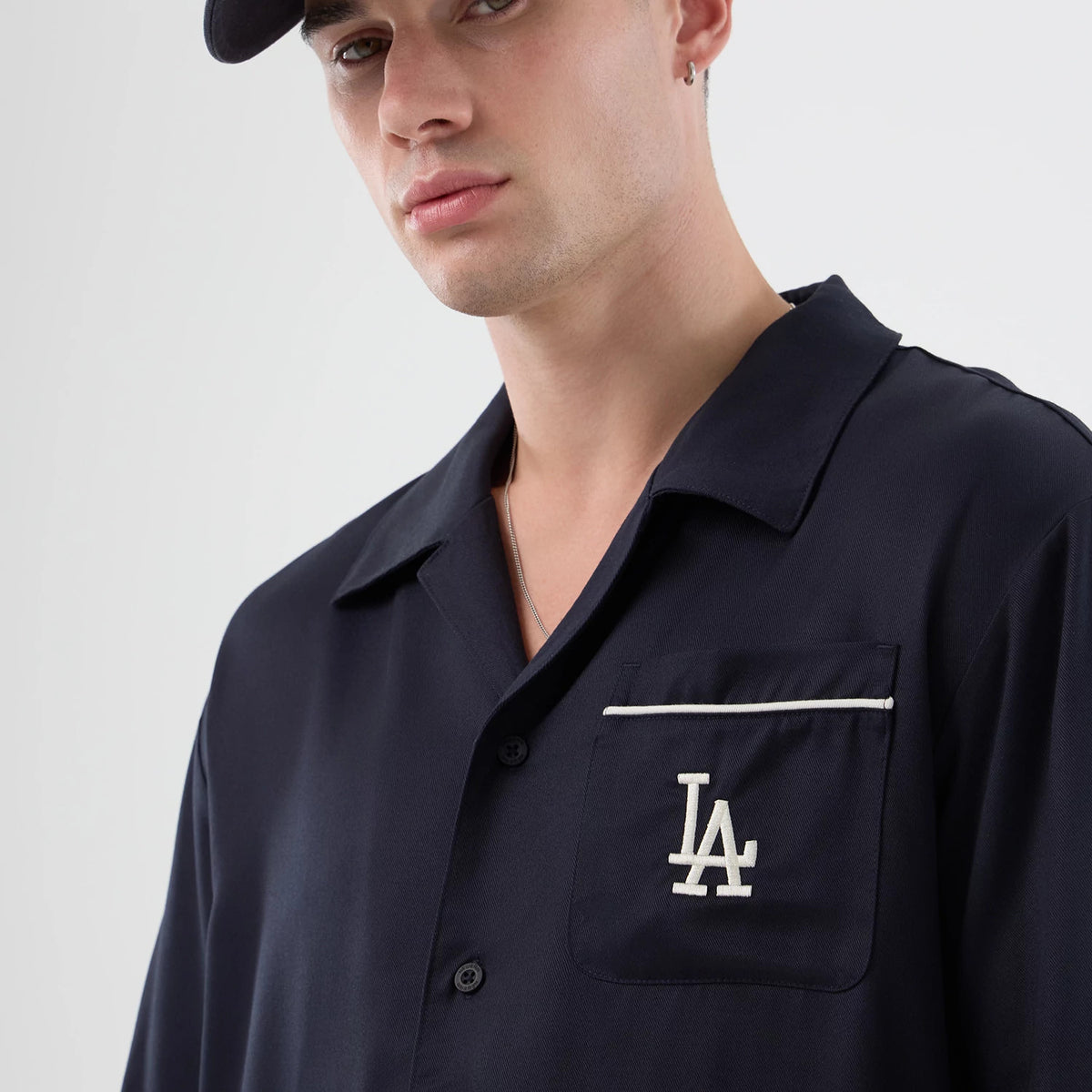 New Era LA Dodgers MLB Graphic Revere Navy Short Sleeve Shirt, front view on a model showing the embroidered white LA logo on the left chest pocket, accented by a contrasting white trim, beneath a classic revere collar.