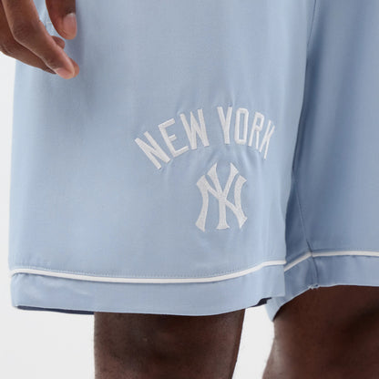 New Era New York Yankees MLB Woven Pastel Blue Shorts, front view showing an embroidered white New York Yankees logo and lettering on the left leg, with a white piping detail running along the hem of the soft blue fabric.