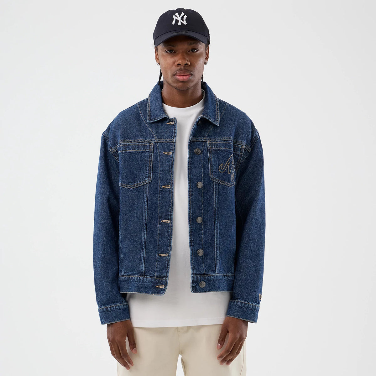 New Era Script Denim Dark Blue Jacket, front view showing a classic denim design with button-up closure, embroidered New Era logo on the left chest, and prominent seams along the chest pockets, worn by a model dressed in neutral tones.