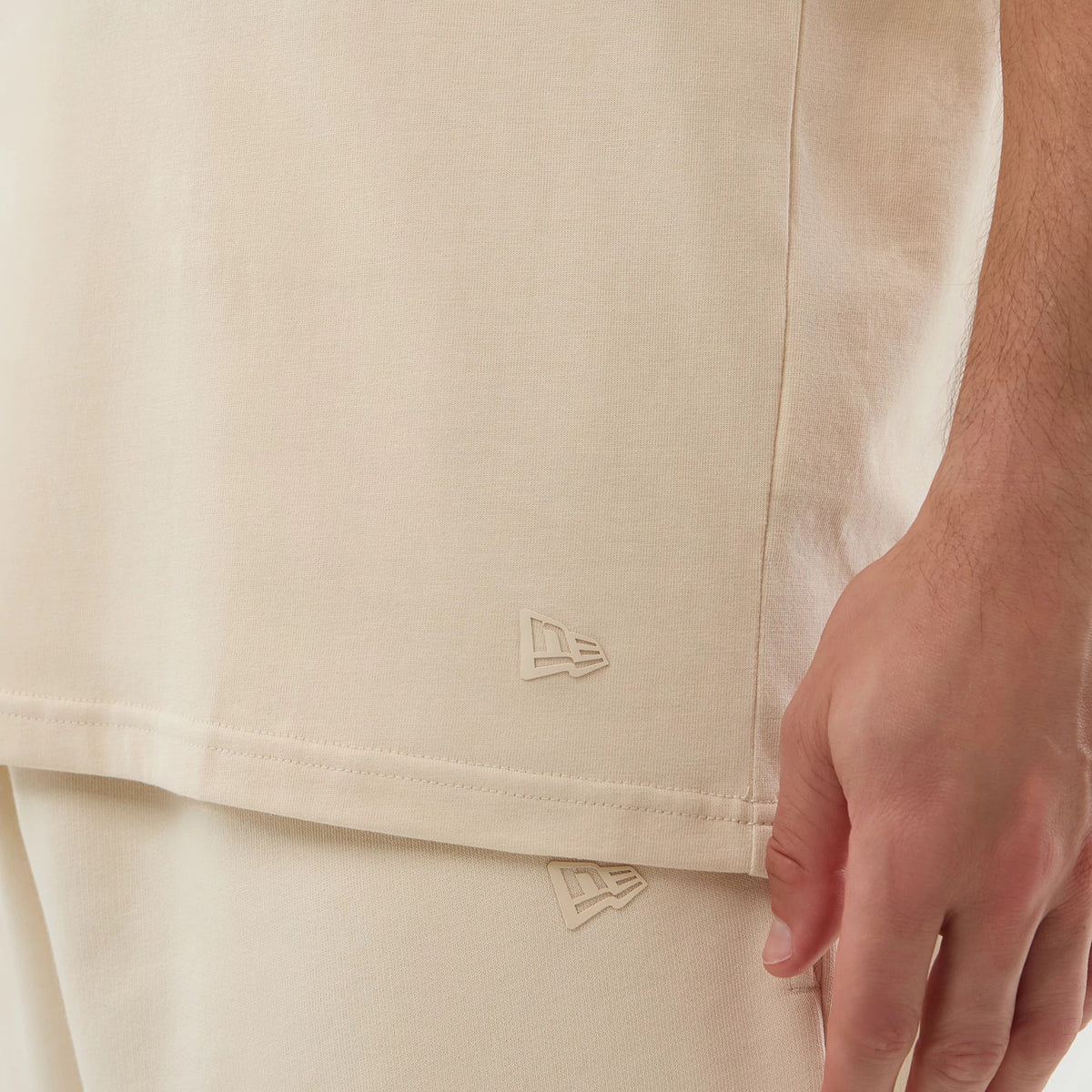 New Era Chicago Bulls NBA Core Plus Light Beige Vest, side view on a model showing the New Era flag logo embroidered near the hem, with the beige fabric appearing and the relaxed fit complementing matching shorts.