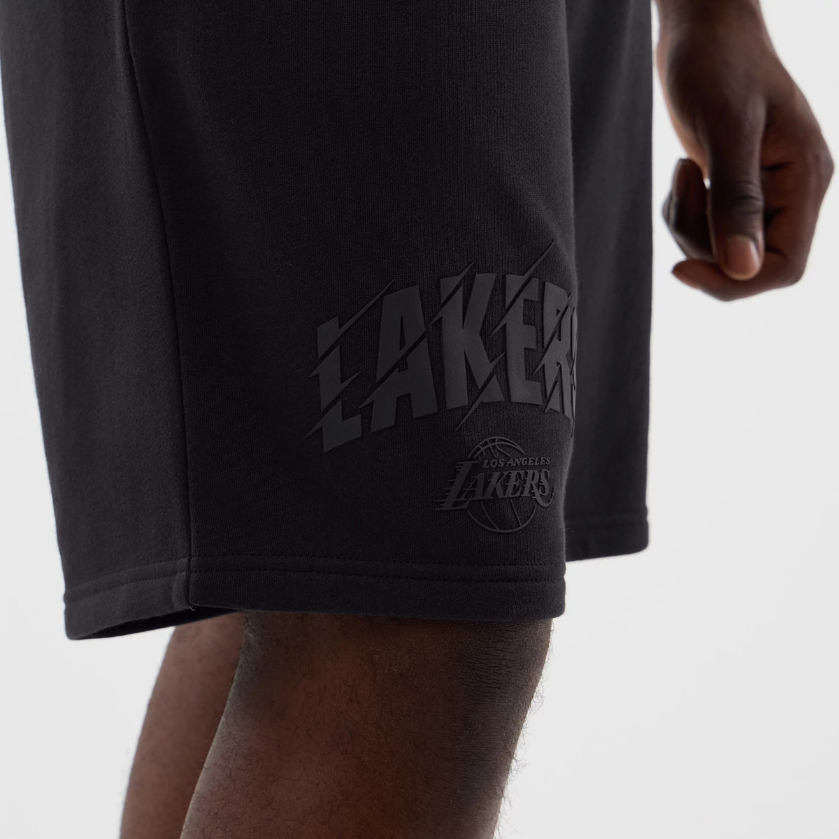 New Era LA Lakers NBA Core Plus Navy Shorts, side view on a model showing an embossed Lakers logo near the hem, a secondary embossed Los Angeles Lakers logo below it, and a clean straight hem for a silhouette.
