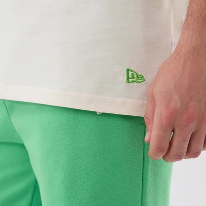 New Era LA Dodgers MLB League Essential Open White Vest, close-up showing the lower hem on a model with a green embroidered New Era flag logo on the left hip, set against bright green trousers for a contrasting look.