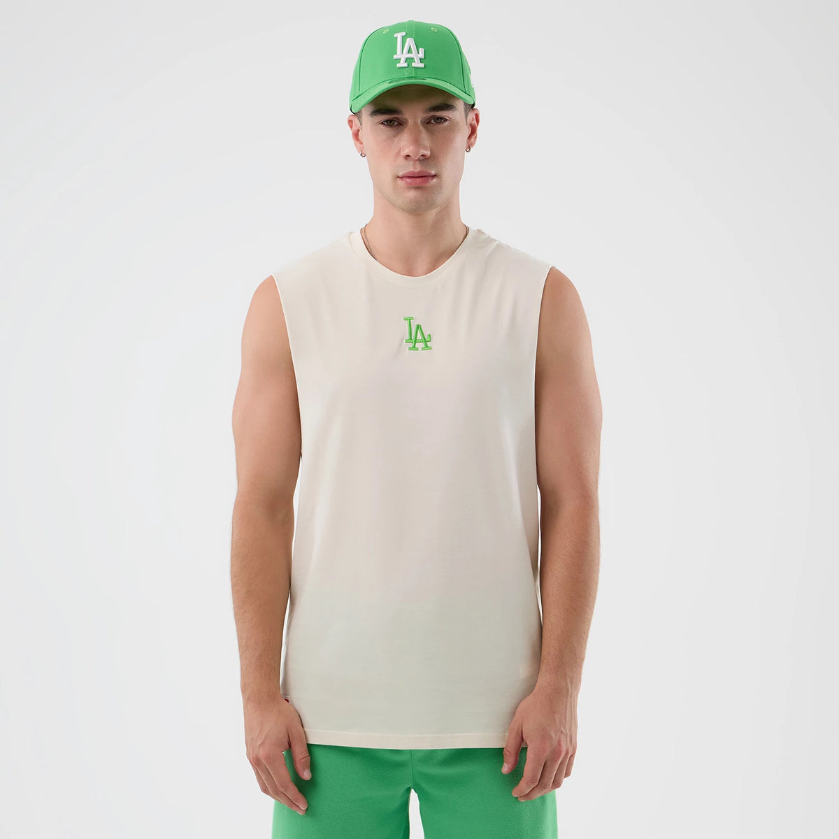 New Era LA Dodgers MLB League Essential Open White Vest, front view on a model with a matching green New Era cap, showing a green LA logo embroidered on the chest, sleeveless design, and relaxed fit.