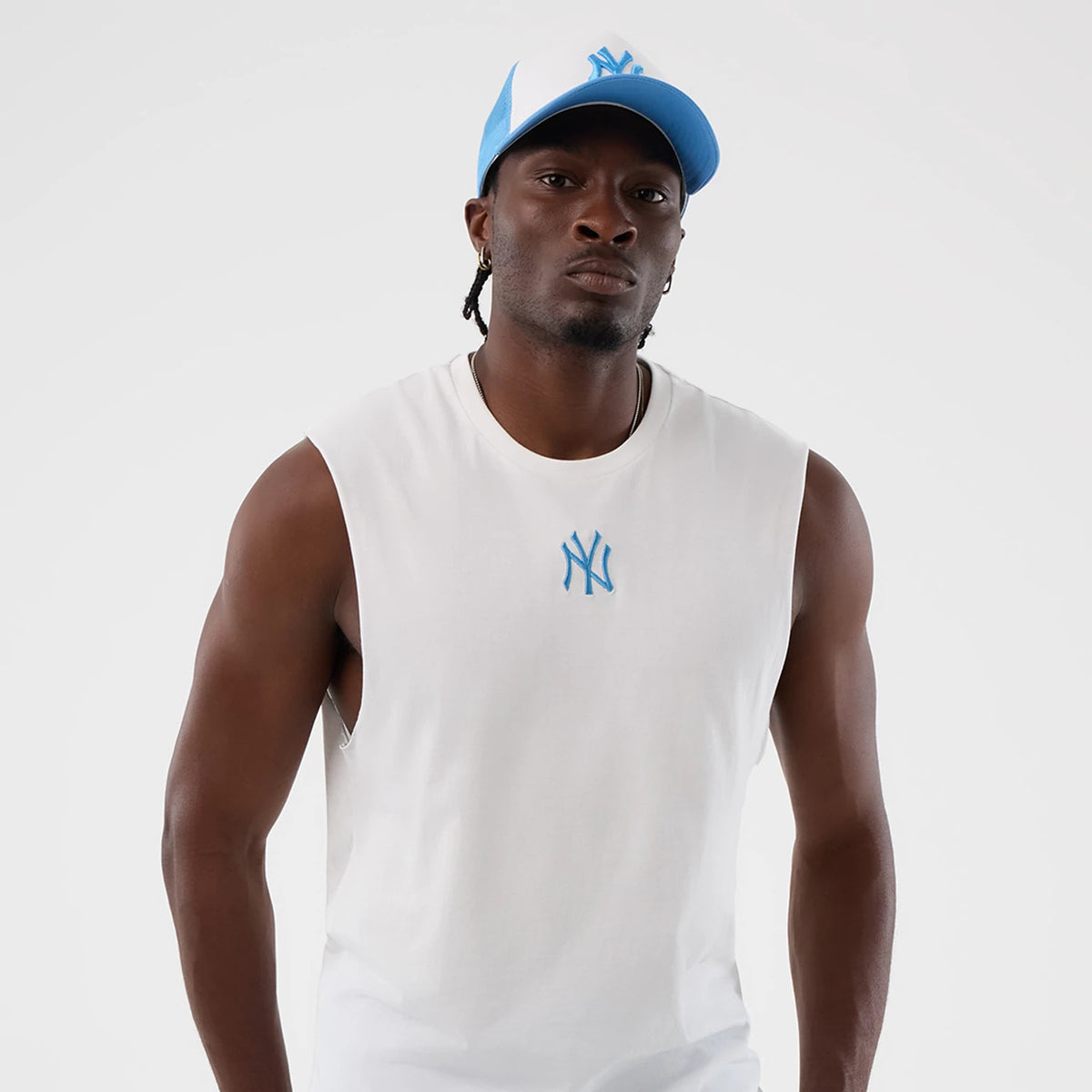 New Era New York Yankees MLB League Essential White Vest, front view on a model with a blue and white cap, showing a prominently embroidered blue NY logo on the chest of the white sleeveless vest.