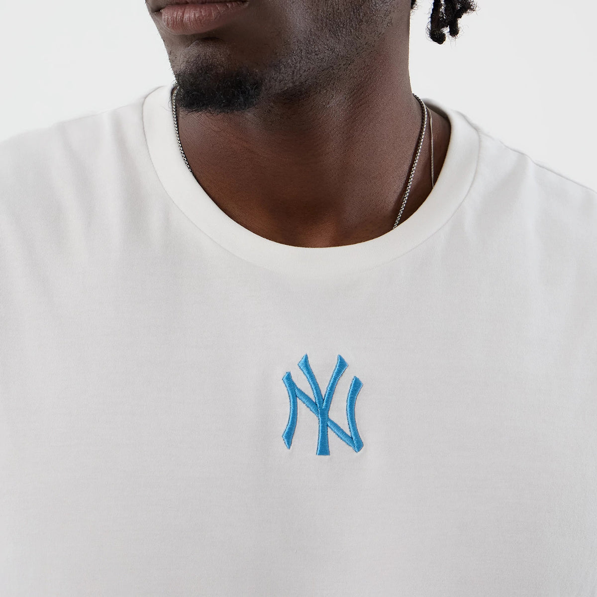 New Era New York Yankees MLB League Essential White Vest, front view on a model, featuring a light blue embroidered NY logo on the chest, a round neckline with a ribbed texture, and white fabric.