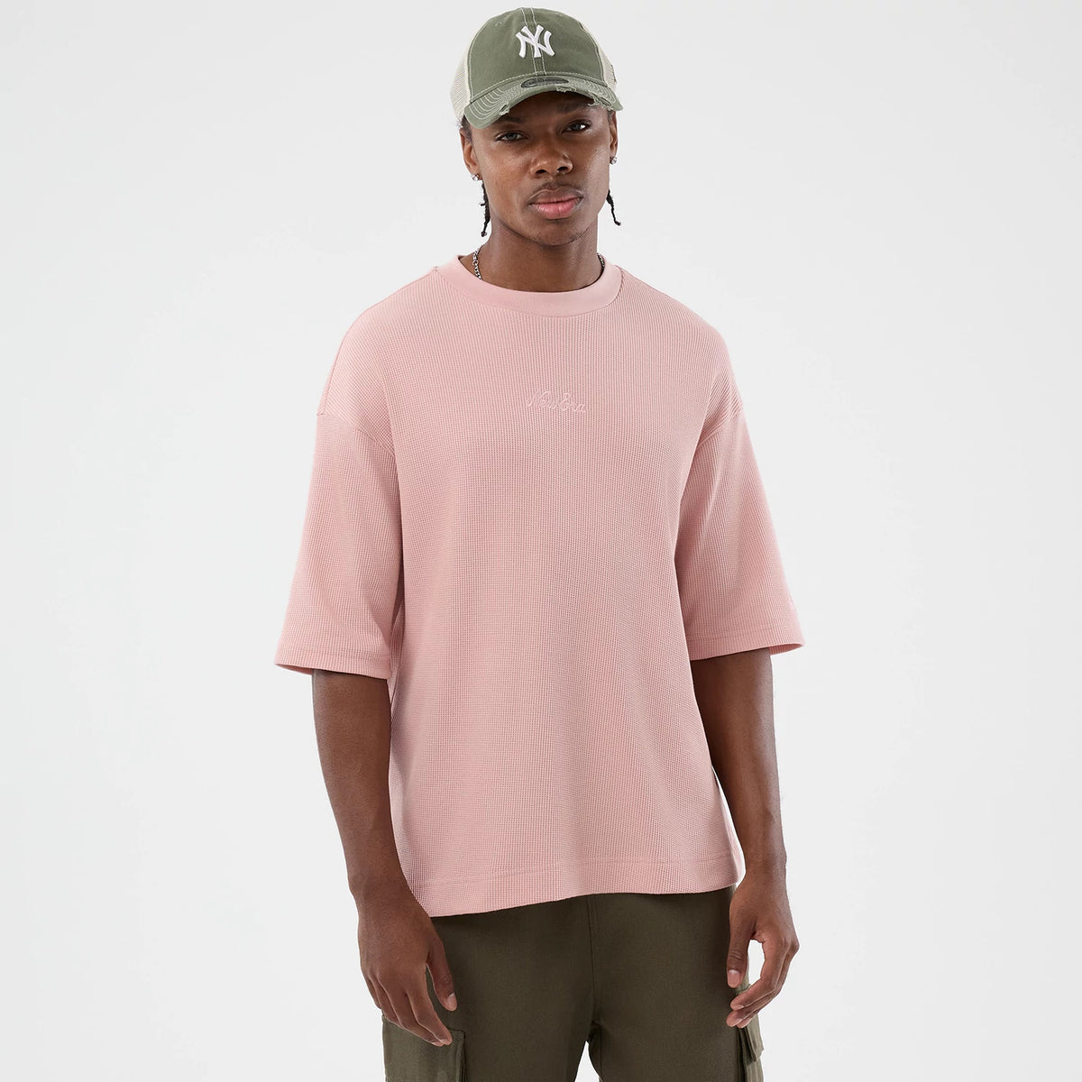 New Era Waffle Pastel Pink T-Shirt, front view on a model styled with an olive cap, showcasing a relaxed fit with elbow-length sleeves and a embossed New Era logo across the chest in matching pastel pink.