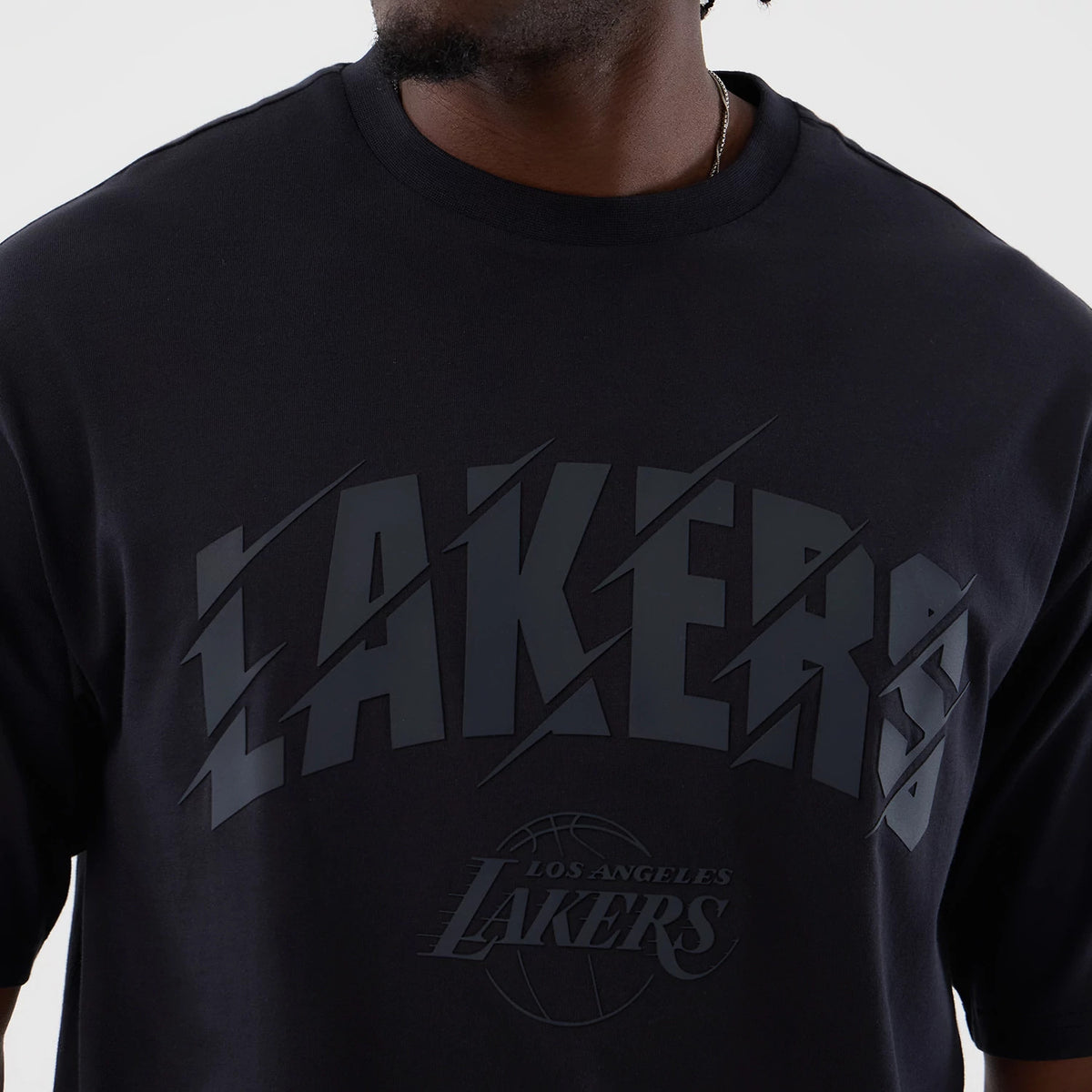 New Era LA Lakers NBA Core Plus Navy Oversized T-Shirt, front view showing oversized navy tee with raised LAKERS text across the chest in dark blue, layered graphic of a basketball beneath, on model with minimal accessories.