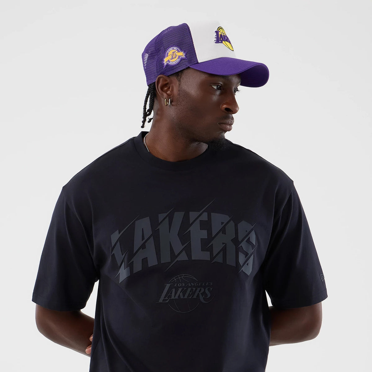 New Era LA Lakers NBA Core Plus Navy Oversized T-Shirt, front view on-model showing a Lakers graphic across the chest, paired with a purple and white cap featuring the Lakers embroidered logo on the front and side.