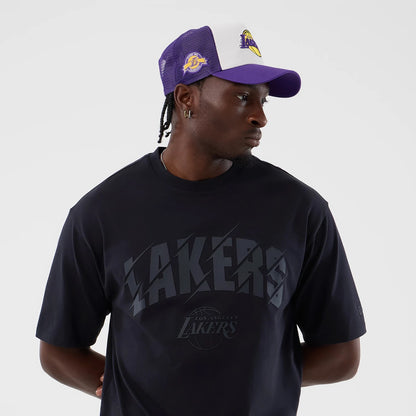New Era LA Lakers NBA Core Plus Navy Oversized T-Shirt, front view on-model showing a Lakers graphic across the chest, paired with a purple and white cap featuring the Lakers embroidered logo on the front and side.