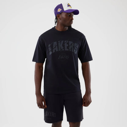 New Era LA Lakers NBA Core Plus Navy Oversized T-Shirt, front view on a model styled with shorts, showing a large Lakers print across the chest and the official team logo beneath, along with dropped shoulder seams for a relaxed fit.