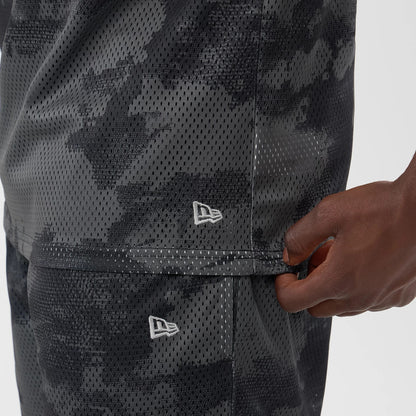 New Era All Over Print Black Camo Mesh Tank Top, side view showing the intricate black camo mesh pattern with two white embroidered New Era flag logos on the lower side, and a person's hand adjusting the hem.
