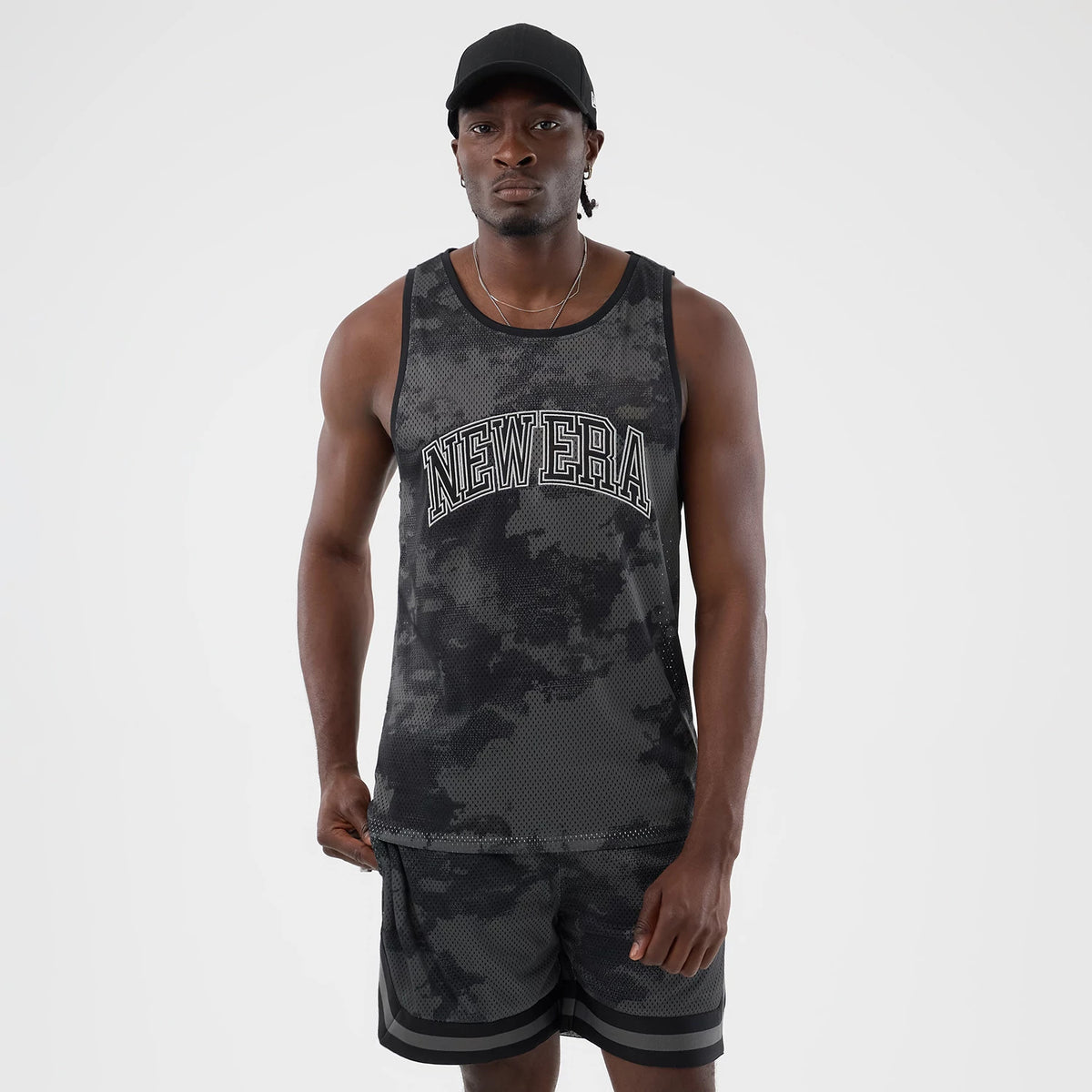 New Era All Over Print Black Camo Mesh Tank Top, front view on a model wearing a black cap, featuring black and grey camo mesh fabric with large white outlined New Era lettering across the chest.