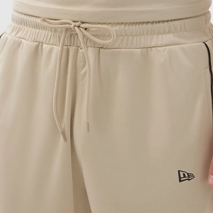 New Era Football Light Beige Shorts, front view showing the light beige colour with an elasticated waistband featuring a drawstring tie at the centre, and a small black embroidered New Era logo positioned on the lower left leg.