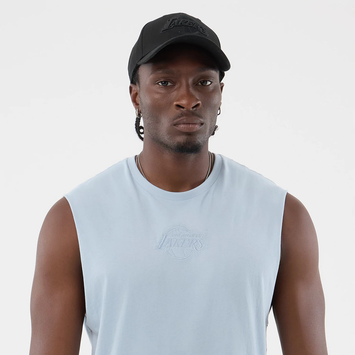 New Era LA Lakers NBA League Essential Pastel Blue Vest, front view on a model with a black cap showing the embroidered Lakers logo on the chest, sleeveless design, and light pastel blue fabric.