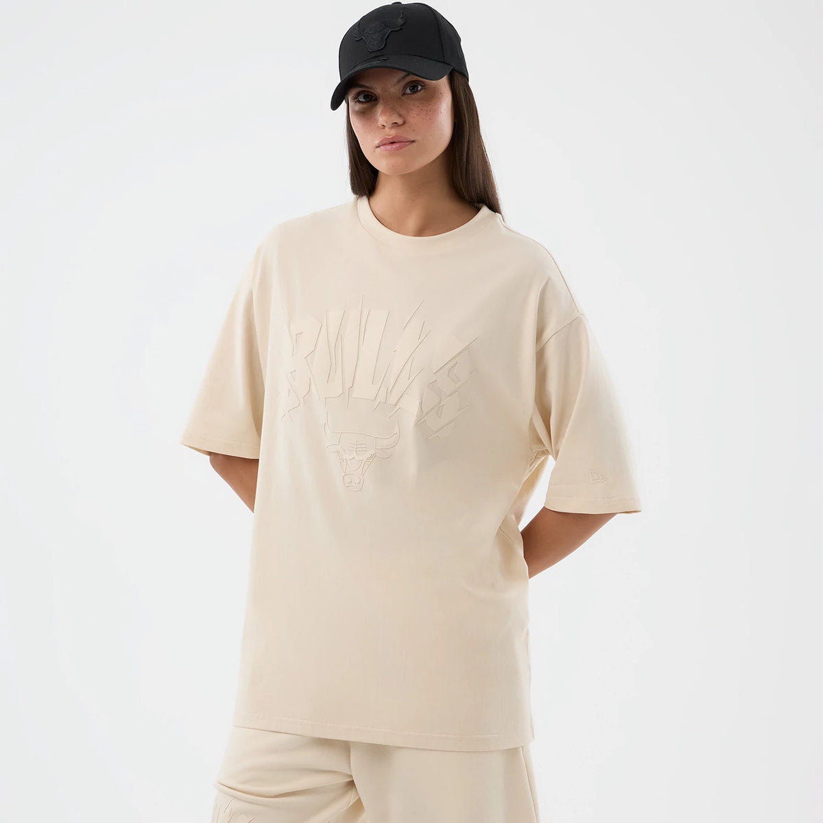 New Era Chicago Bulls NBA Core Plus Light Beige Oversized T-Shirt, front view on-model displaying a light beige oversized fit, a debossed Bulls logo graphic on the chest, and a New Era flag embroidered on the left sleeve.