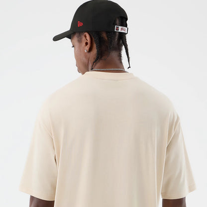 New Era Chicago Bulls NBA Core Plus Light Beige Oversized T-Shirt, back view on-model showcasing the plain light beige oversized design with short sleeves, styled with a black cap featuring embroidered red Bulls branding above the adjustable strap.