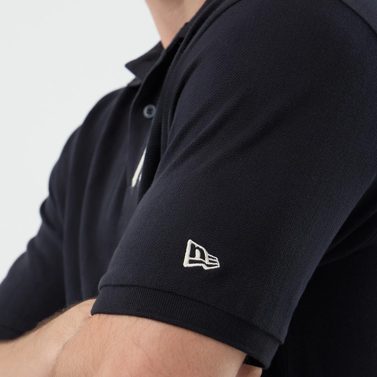 New Era New York Yankees MLB Rib Navy Polo T-Shirt, side view showing a short-sleeved design with a white embroidered New Era logo on the left sleeve, and a button-up collar styled on a model with crossed arms.