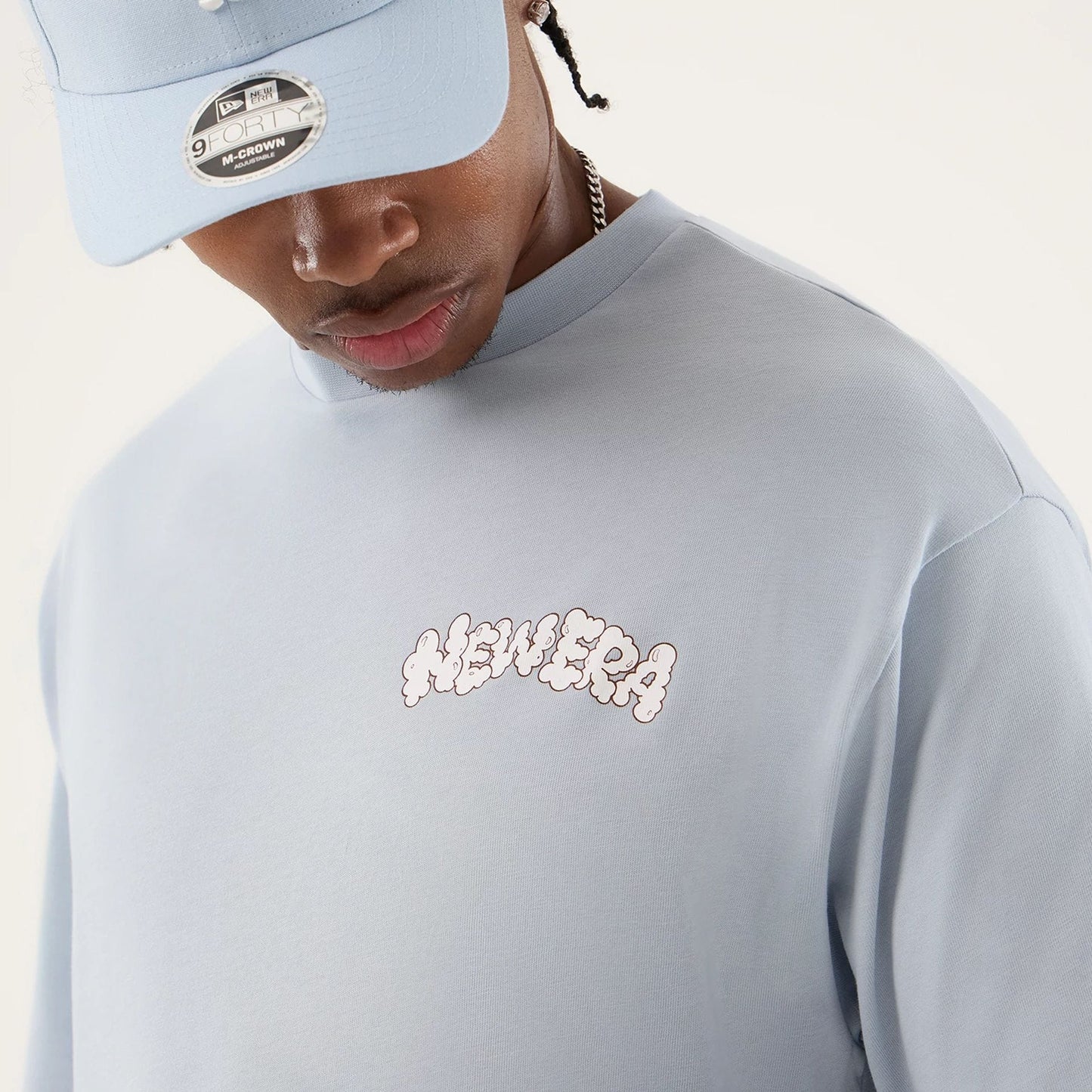 The model is wearing this New Era Fun Block Party Graphic Oversized T-Shirt in pastel blue. 5