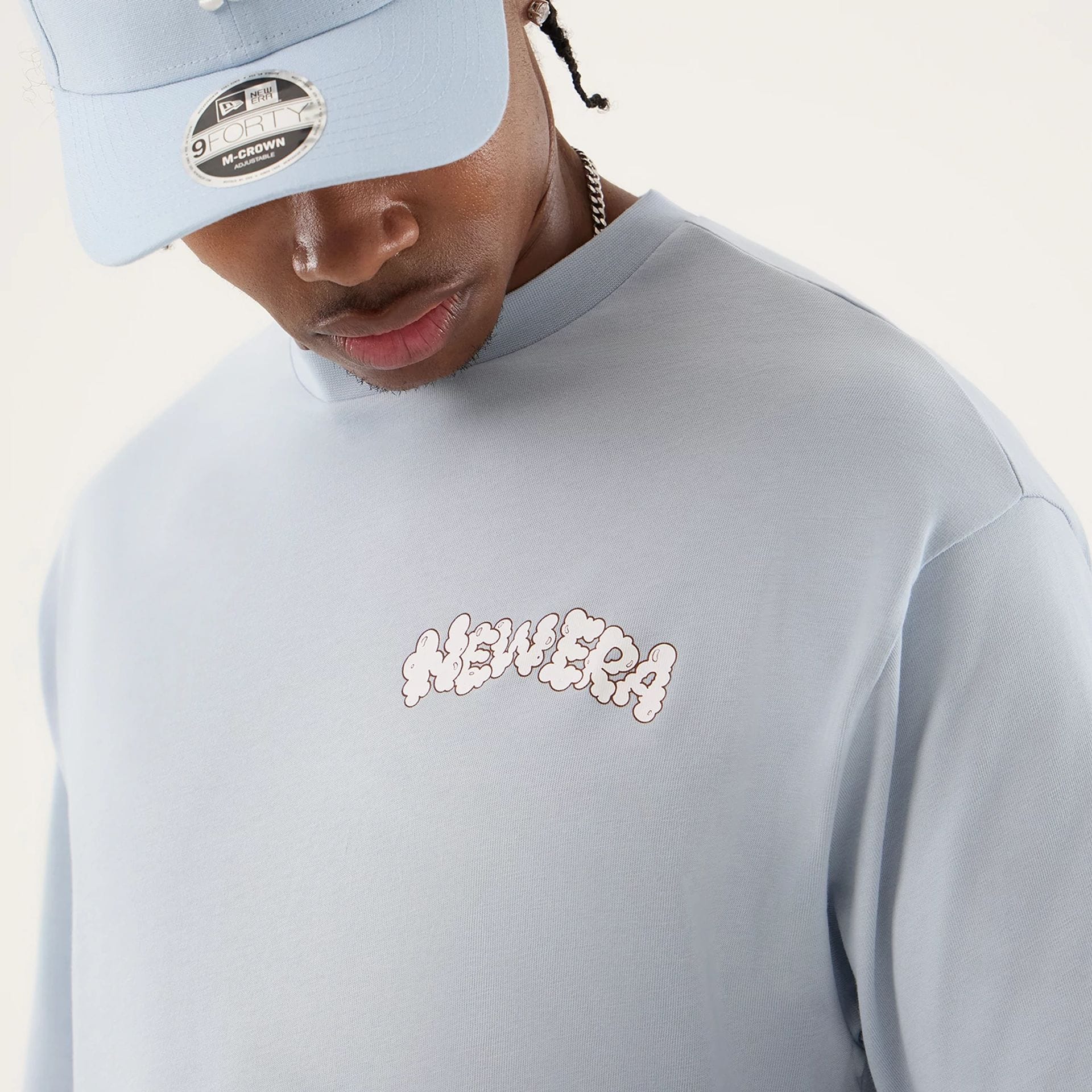 The model is wearing this New Era Fun Block Party Graphic Oversized T-Shirt in pastel blue. 5