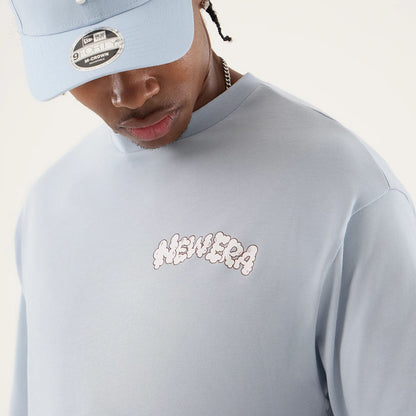 The model is wearing this New Era Fun Block Party Graphic Oversized T-Shirt in pastel blue. 5