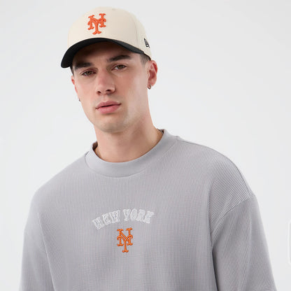 New Era New York Mets MLB Waffle Grey T-Shirt, front view on a model wearing a matching cap, featuring New York lettering and an orange embroidered Mets logo centred on the chest, with a textured waffle pattern throughout the grey fabric.