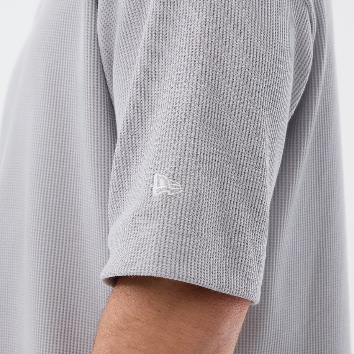 New Era New York Mets MLB Waffle Grey T-Shirt, side view showing a textured grey fabric with a white embroidered New Era logo on the sleeve, short sleeves and a relaxed fit on a model’s arm, highlighting the intricate waffle pattern.