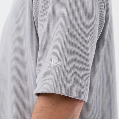 New Era New York Mets MLB Waffle Grey T-Shirt, side view showing a textured grey fabric with a white embroidered New Era logo on the sleeve, short sleeves and a relaxed fit on a model’s arm, highlighting the intricate waffle pattern.