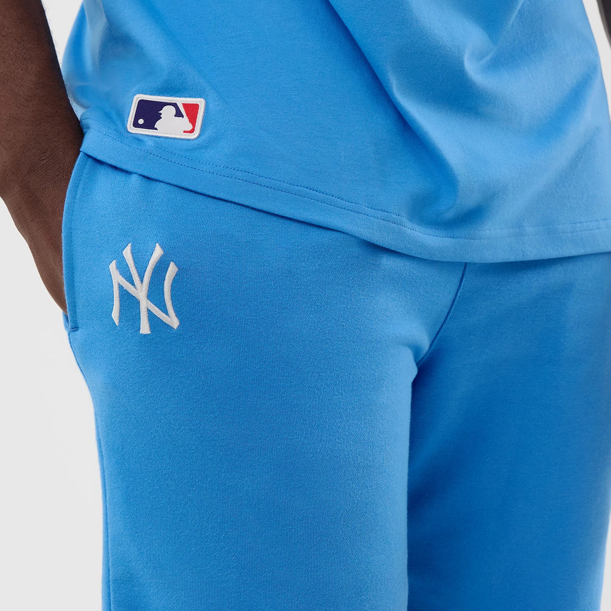 New Era New York Yankees MLB League Essential Pastel Blue Shorts, close-up side view showing the white embroidered NY logo on the left thigh, a small MLB logo on the matching shirt above the shorts, and the pastel blue fabric design.